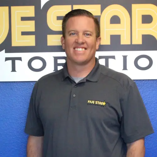 Kevin webp A person in a dark gray polo shirt stands in front of a large "Five Star" sign against a blue wall.
